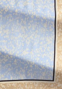 Zijden sjaal met een lichtblauwe achtergrond en een crèmekleurig abstract patroon, omlijnd met een beige rand en een dunne zwarte lijn.