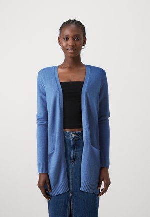 Cardigan blu realizzato in morbido tessuto, con apertura frontale, due tasche anteriori e polsini a costine. Indossato sopra un top nero e una gonna di jeans.