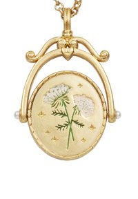 Zlatý náhrdelník s príveskom v kvetinovom dizajne so bielymi a zelenými akcentmi, obklopený malými hviezdami a pripojený na textúrovaný reťazec.