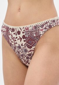 Μπικίνι κάτω μέρος σε εκρού χρώμα με μοτίβα λουλουδιών σε μαρονα και μπλε. Διαθέτει κυματοειδείς άκρες, μαλακό ύφασμα και σχέδιο με χαμηλή μέση.