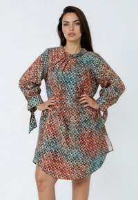Vloeiende, multicolore jurk in aardetinten met een patroon van ovale vormen. Heeft lange mouwen en strikaccenten bij de manchetten.