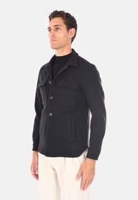 Giacca nera in lana con colletto, bottoni frontali, due tasche sul petto e tasche laterali. Tessuto morbido e vestibilità su misura.