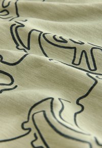 Tej alakú, krém színű anyag fekete, absztrakt vonalmintákkal, amely lágy textúrával és sima, enyhén gyűrött felülettel rendelkezik.