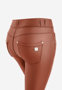 Leggings marrones con una textura suave, de cintura alta, y dos bolsillos traseros con herrajes plateados y costuras detalladas.