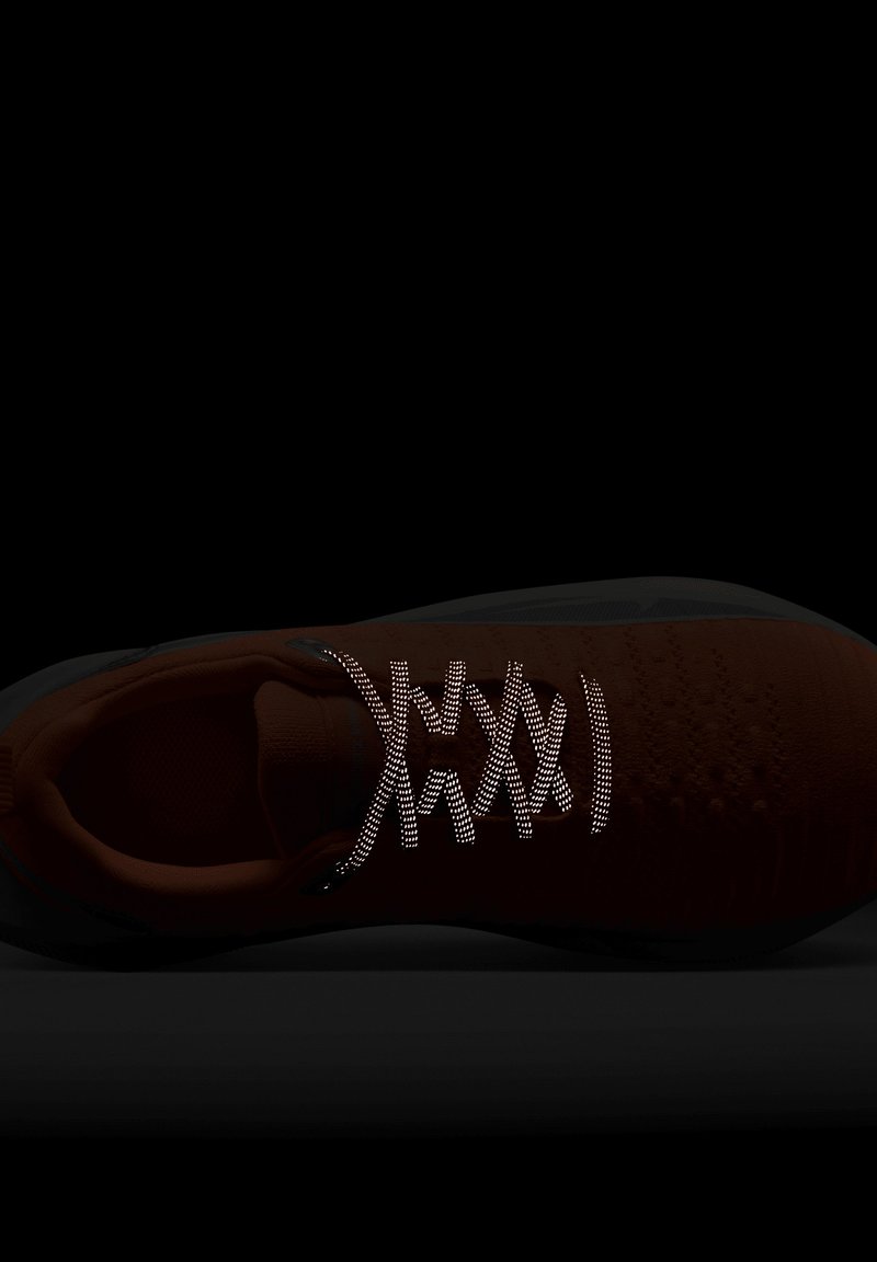 Czerwony but sportowy z teksturowaną cholewą, odblaskowymi sznurówkami i czarną podeszwą. Projekt charakteryzuje się bezszwową konstrukcją dla zapewnienia komfortu.