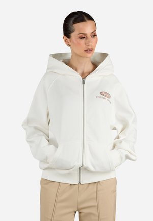 Biela zip-up mikina s voľným strihom, s veľkou kapucňou, prednými vreckami a malým vyšívaným logom na hrudi. Hladká textúra.