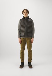 Sort puffer vest over en grå langærmet top, parret med olivengrønne bukser og sorte støvler. Simpelt design, glat tekstur og praktisk styling.