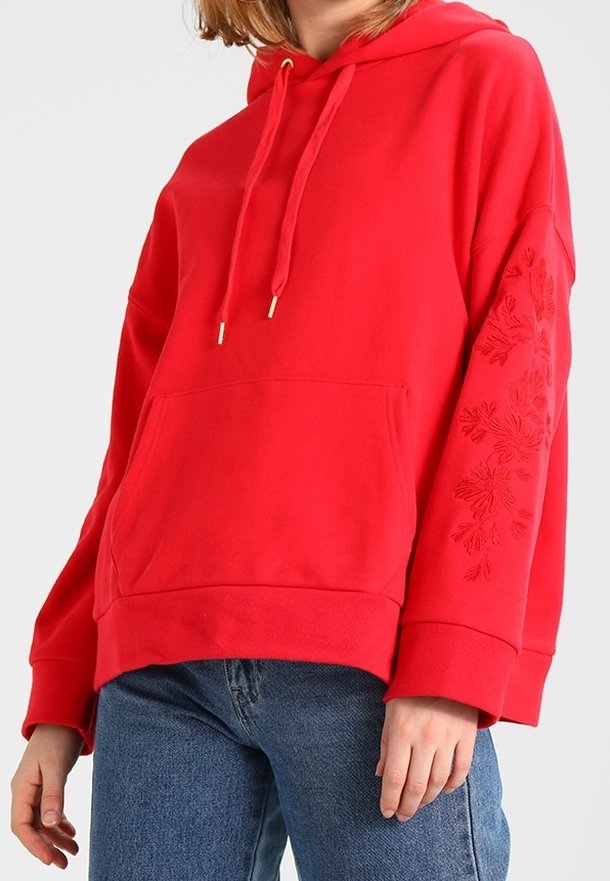 Sudadera con capucha roja con un bolsillo canguro, bordado floral texturizado en la manga izquierda y cordón ajustable. Tela suave, corte relajado.