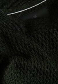 Primo piano di un maglione lavorato a maglia verde scuro che mostra il collo a costine e il motivo lavorato a maglia strutturato con una piccola etichetta nera in tessuto all'interno.