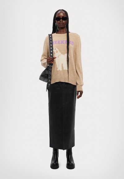 Maglione lavorato a maglia beige con il testo "WEEKEND" e un design di cane. Abbinato a una gonna maxi in pelle nera e stivali neri chunky. Presente una borsa a tracolla nera.