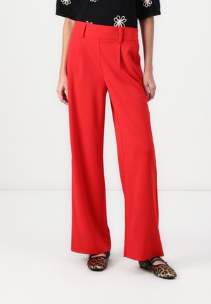 Red wide-leg trousers with a smooth texture, flat front pleats, and a tailored waistband, paired with printed shoes.