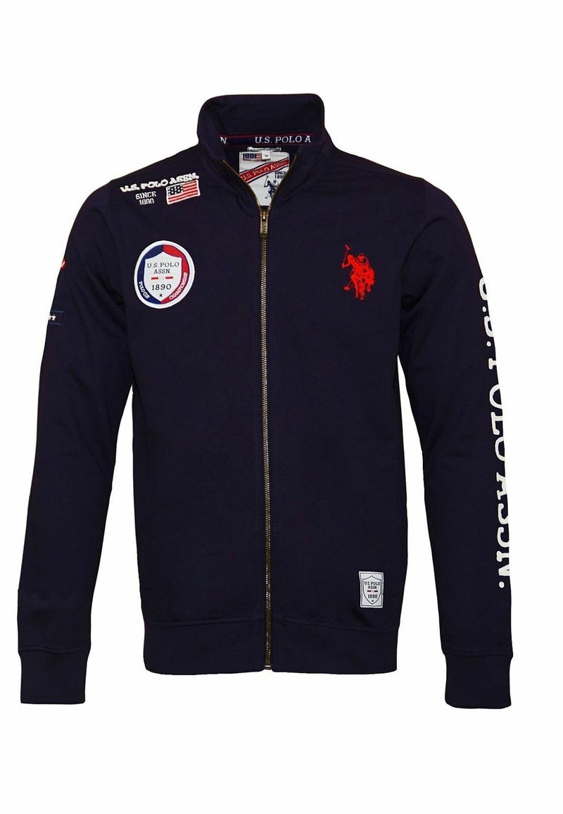 Veste zippée marine avec logo joueur de polo rouge, écussons U.S. Polo Assn., et texte blanc sur la manche droite.