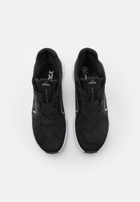 Zapatos deportivos negros con una parte superior de malla transpirable, que presentan un acabado texturizado, suela blanca y acentos en blanco y gris contrastantes.