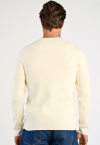 Rippstrickpullover in hellem Creme mit langen Ärmeln und Rundhalsausschnitt. Das Material hat eine weiche Textur mit dezentem Stretch.