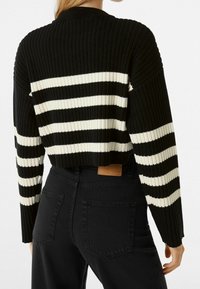 Czarnobiały, prążkowany sweter w paski z długimi rękawami i okrągłym dekoltem, zestawiony z wysokim stanem czarnych jeansów z tylnymi kieszeniami.