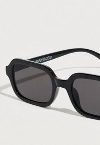 Μαύρα γυαλιά ηλίου με παχύ πλαστικό σκελετό, ορθογώνια φακούς και γυαλιστερό φινίρισμα. Φέρουν την επωνυμία «even&odd» στο εσωτερικό του βραχίονα.