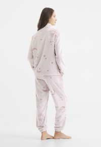 Conjunto de loungewear de forro polar en rosa claro con patrones celestiales. La parte superior cuenta con un alto cuello y los pantalones tienen puños elásticos para mayor comodidad.