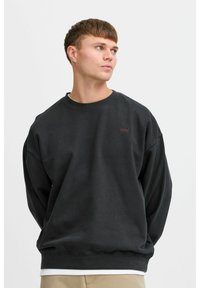 Mørkegrå genser med rund hals, senkede skuldre og lange ermer. Har en liten brodert logo i en kontrastfarge. Myk tekstur.