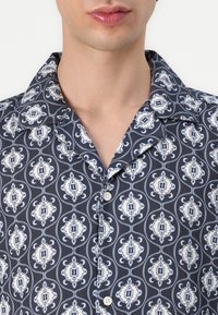 Camicia blu navy con bottoni, caratterizzata da un motivo ornato bianco e azzurro chiaro, con colletto classico e maniche corte, realizzata in tessuto liscio.