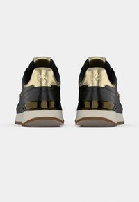 Μαύρα αθλητικά παπούτσια με γυαλιστερές χρυσές λεπτομέρειες. Διαθέτουν υφασμένο επάνω μέρος, στρογγυλεμένο σχήμα και παχύ λευκό πέλμα με καφέ λαστιχένιο κάτω μέρος.