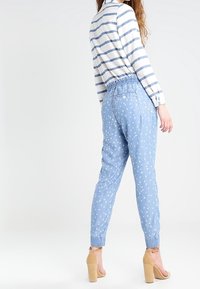 Hellblaue Jeanshose mit entspanntem Schnitt und elastischem Bund, ausgestattet mit einem weißen Blumenmuster und aufgerollten Säumen.