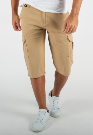 Shorts cargo beiges avec deux poches latérales, une coupe décontractée et des détails cousus, associés à des sneakers blanches.