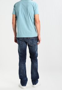 Modré bavlněné tričko s krátkými rukávy, spárované s tmavými modrými džíny. Viditelné bílé tenisky, džíny mají zadní kapsy se švy.