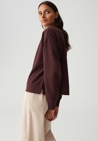 Bordeaux sweatshirt met een relaxed fit, geribbelde boorden en zijsplitten. G gedragen met beige, gestructureerde wijde broek.