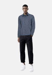 Camicia a maniche lunghe blu navy con un piccolo motivo floreale bianco, abbinata a pantaloni neri alla caviglia e sneakers bianche. Tessuto morbido con una vestibilità comoda.
