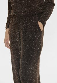 Bruin, zacht stoffen jumpsuit met een relaxte pasvorm, lange mouwen en verspreide witte en zilveren glitters, met zijzakken voor extra functionaliteit.