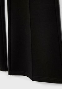 Primo piano di pannelli di tessuto nero con orli doppi cuciti dritti ai bordi, che mostrano una texture liscia e la costruzione del capo.