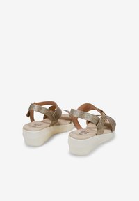 Sandales strappy métalliques dorées avec une semelle intérieure beige rembourrée et une semelle blanche en plateforme. Présente un accent de boucle sur la sangle.
