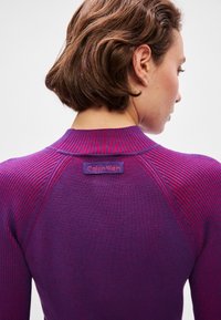 Suéter roxo com textura em fita e um design ajustado, apresentando uma etiqueta da Calvin Klein na gola e detalhes de listras contrastantes nos ombros.