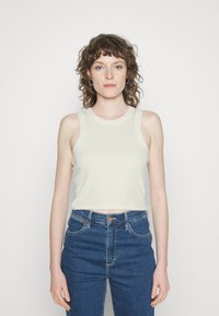 Top cropped de cor clara, com textura canelada, gola redonda e design sem mangas, combinado com jeans de cintura alta em denim azul.