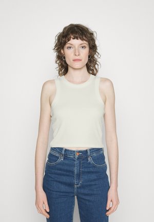 Top cropped de cor clara, com textura canelada, gola redonda e design sem mangas, combinado com jeans de cintura alta em denim azul.