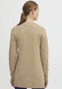 Beige kötött pulóver hosszú ujjakkal, bordás mandzsettával és szegéllyel. Kerek nyakkivágással és laza fazonnal rendelkezik, puha anyagból készült.
