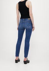 Smala blå jeans med en blekt finish, bakfickor och en tan läderetikett ovanför midjan, kombinerat med en svart ärmlös topp.