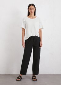 White short-sleeve t-shirt with a pocket, paired with loose black pants, and black sandals with two straps and a gold buckle detail.