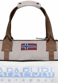 Borsa da viaggio in tela grigia chiara con manici marroni, caratterizzata da una toppa con la bandiera norvegese e un logo blu del marchio. Chiusura con zip nella parte superiore.