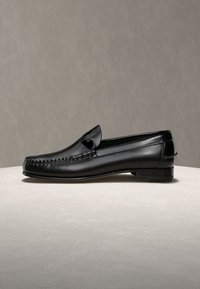 Mocassin pour homme en cuir noir avec couture moc toe, petit talon et fente pour pièce, présenté de profil sur une surface neutre.