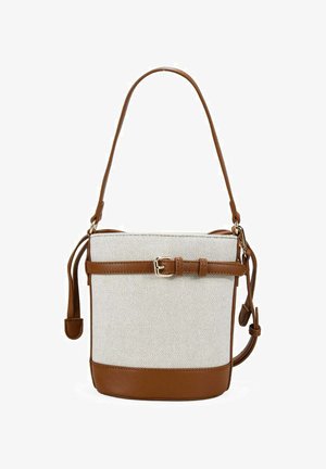 Bolso de lona beige tipo bucket con ribete de cuero marrón, correa de hombro ajustable y cinturón decorativo en la parte delantera.