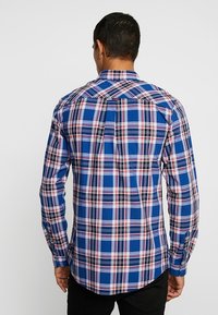 Koszula w kratę w odcieniach niebieskiego, białego i czerwonego. Długie rękawy zakończone mankietami na guziki oraz klasyczny kołnierz.