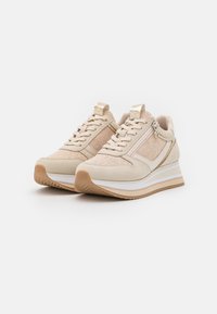 Chaussures de sport beige avec une tige en mesh texturé, lacets, fermeture éclair latérale et semelle en caoutchouc épaisse avec une bande d'accent blanche.