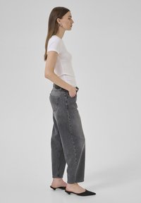 T-shirt blanc ajusté, jeans noirs taille haute avec une coupe décontractée, et chaussures noires à enfiler à talons pointus. Design simple sans motifs visibles.