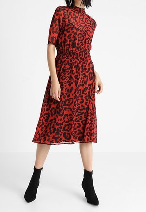 Nainen, jolla on punainen midi-mekko mustalla leopardikuvioinnilla, lyhyet hihat, joustava vyötärö, yhdistettynä mustiin nilkkureihin.