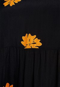 Musta kangasmekko, jossa on kirkkaan oransseja kukkakuoseja ja pleatattu muotoilu hameessa. Rakennepinta tuo syvyyttä ilmeeseen.