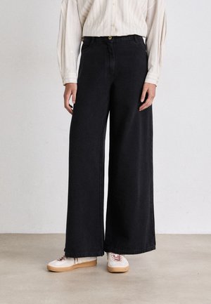 Wide-leg black jeans made of denim with a smooth texture. Features a button closure, and paired with white sneakers with red accents.