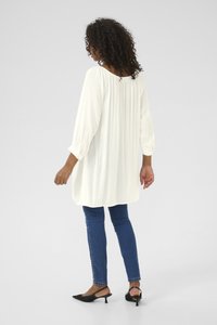Weiße Bluse mit langen Ärmeln, plissierter Textur, lässiger Passform und Rundhalsausschnitt, kombiniert mit dunkelblauen Skinny Jeans und schwarzen Slingback-Schuhen.