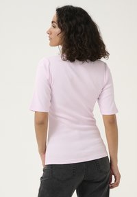 Lilafärgad figurnära t-shirt med korta ärmar, ribbat mönster och rund halsringning, parat med mörk denimjeans, visad i sidovy.