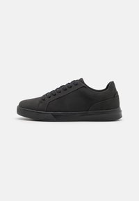 Chaussures de sport noires avec une texture lisse, un bout arrondi, une semelle intercalaire contrastante et des lacets noirs. Design minimaliste, adapté à un usage décontracté.